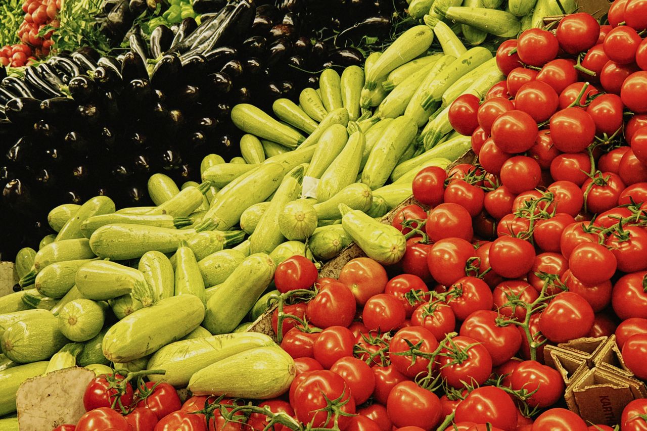 Colorful assortment of fresh vegetables including zucchini, tomatoes, and eggplants at a farmers market display.